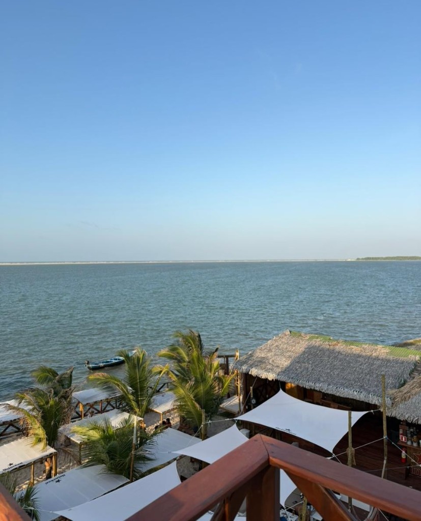 Vista do deck elevado com guarda-sóis, palmeiras e mar ao horizonte em Atins