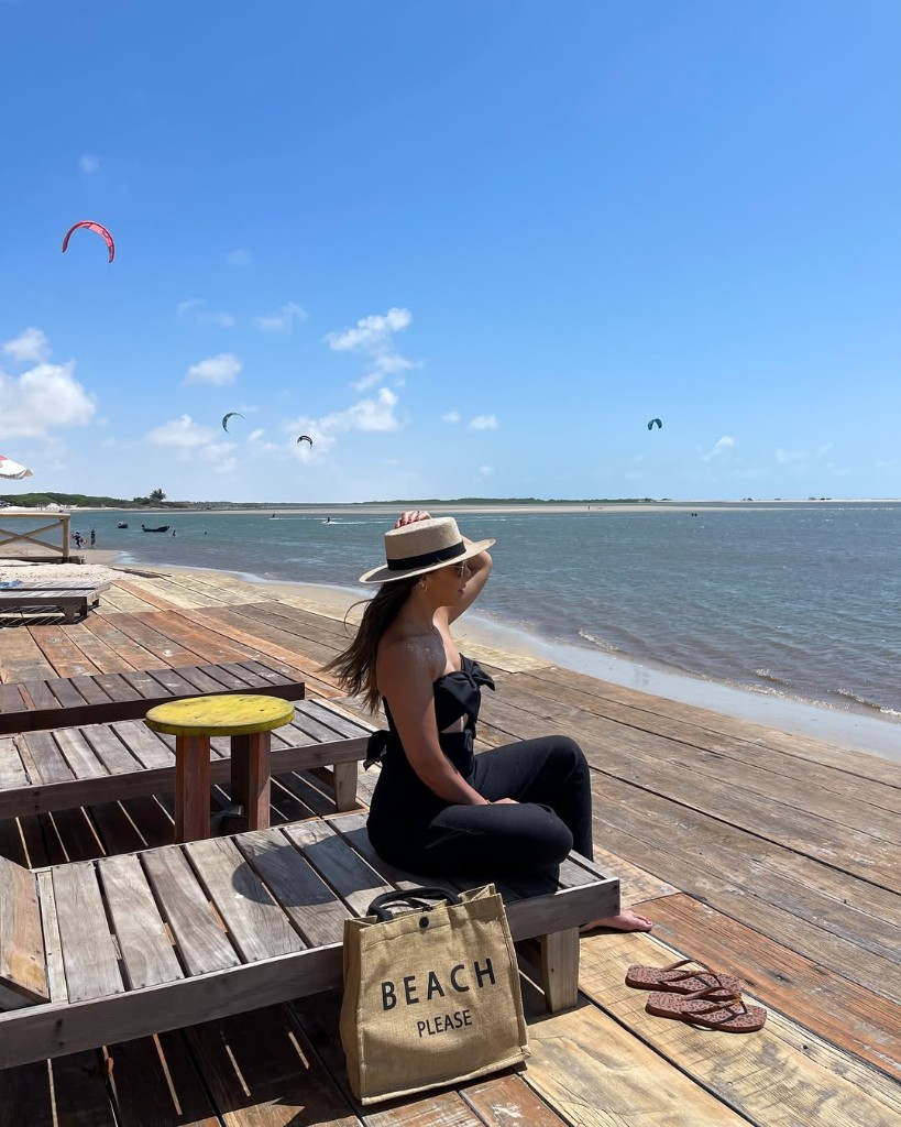 Mulher em espreguiçadeira no deck com vista para kitesurf ao longe