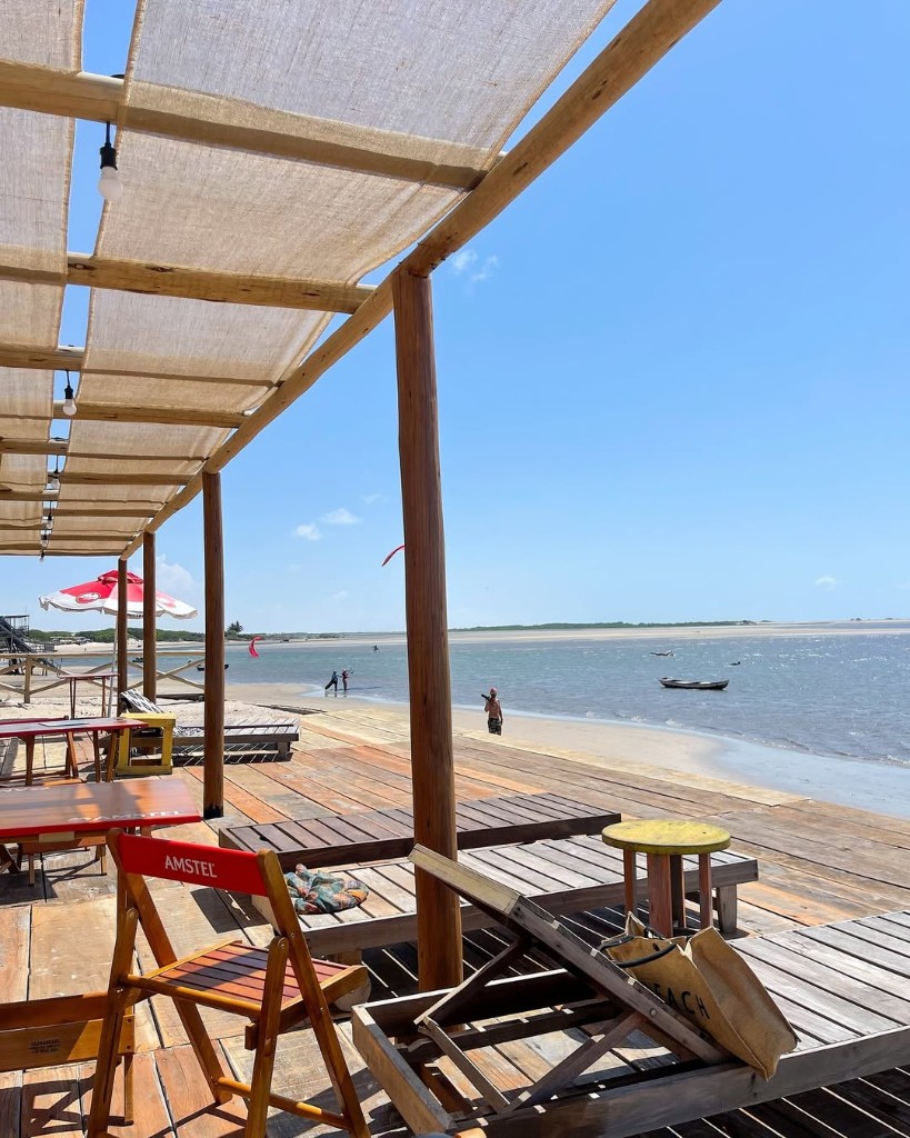 Deck rústico com espreguiçadeiras e vista para praia e pipas no céu em Atins