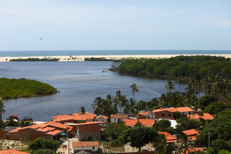Vista de Caburé e casas com telhado laranja às margens do Preguiças, dunas e oceano