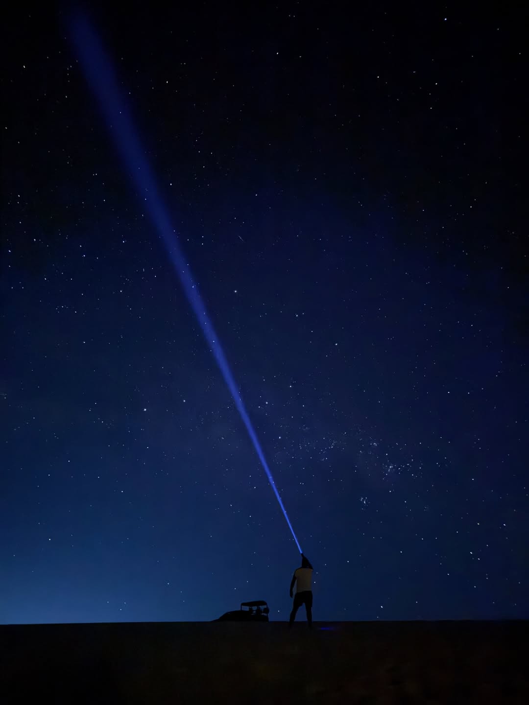 Pessoa apontando feixe de luz azul para o céu estrelado nas dunas