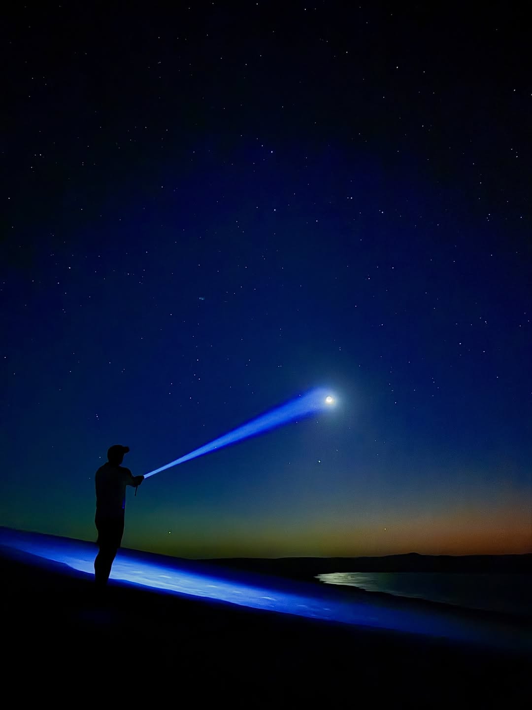 Silhueta com luz azul apontada para a lua em cenário noturno