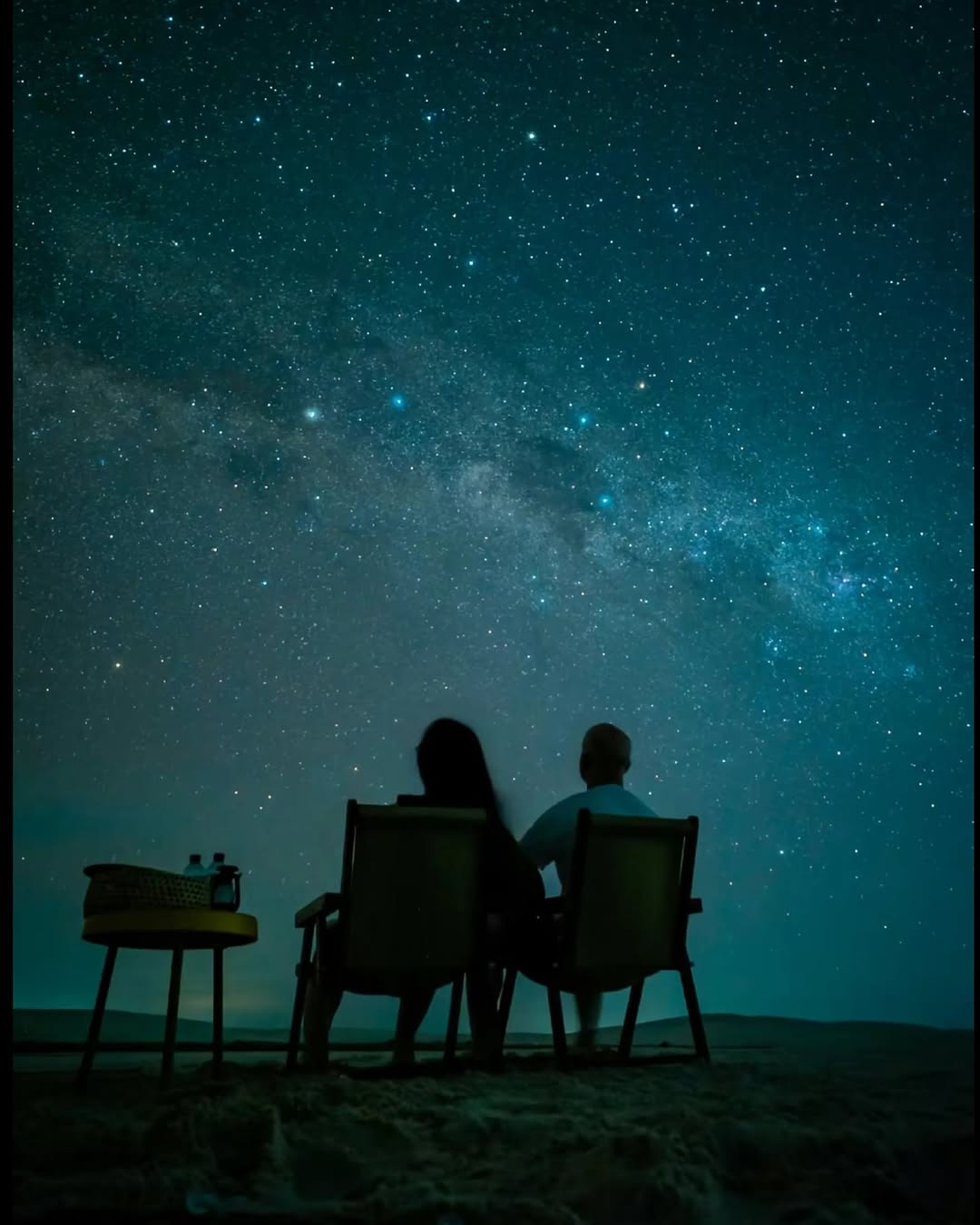 Casal sentado contemplando o céu estrelado sobre as dunas