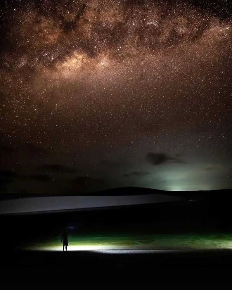 Pessoa iluminada em duna com céu carregado de estrelas