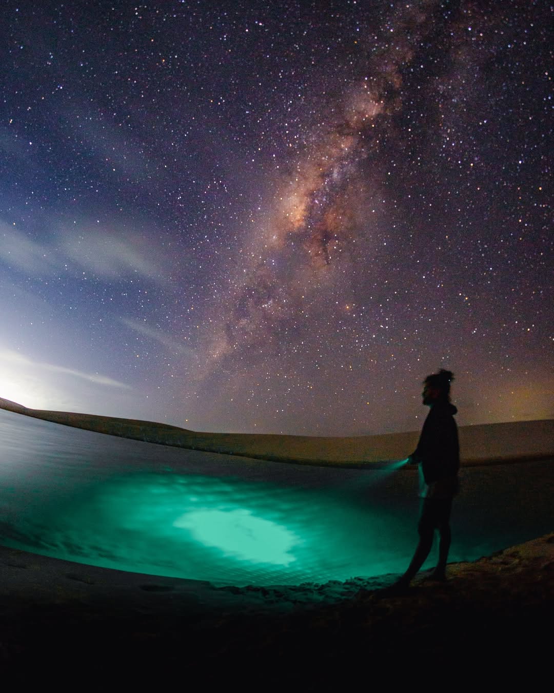 Pessoa ao lado de lagoa azul iluminada durante o passeio noturno