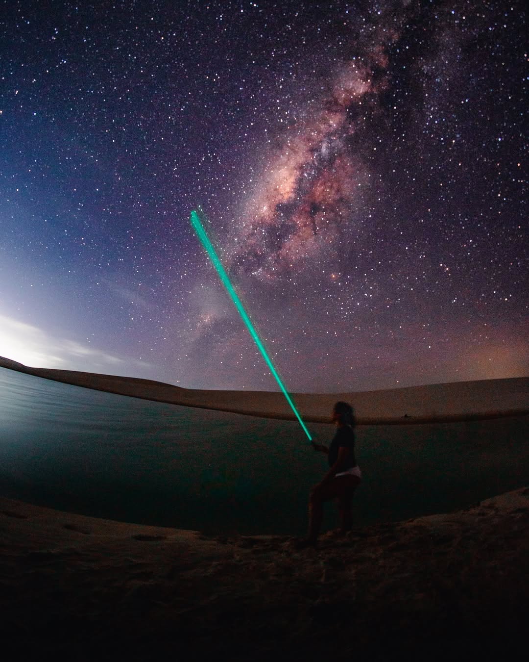 Visitante nas dunas com feixe verde apontado para o céu estrelado