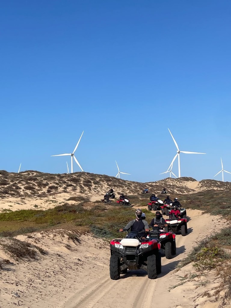 Grupo de quadriciclos em trilha com aerogeradores ao fundo